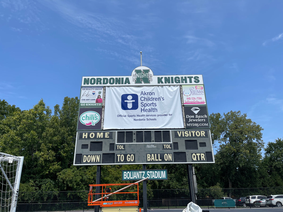 New 13 oz Banner in the beginning stages of installation on massive backlit scoreboard