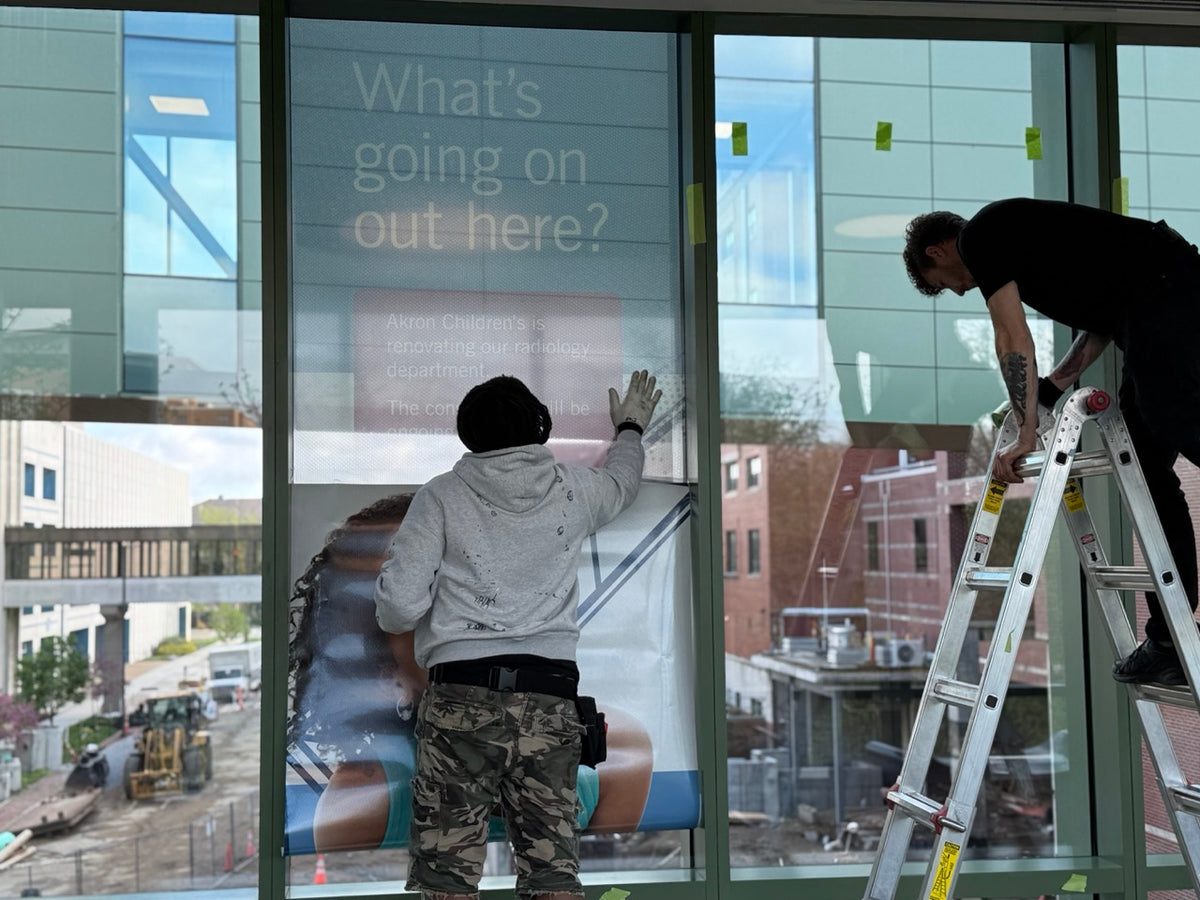 DG Creativ Installers applying window perf graphics with an optically clear over laminate on one of Akron Children's Hospital pedestrian bridges