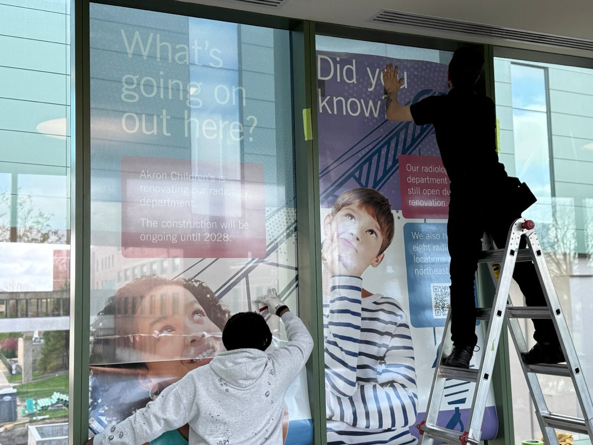 DG Creativ Installers applying window perf graphics with an optically clear over laminate on one of Akron Children's Hospital pedestrian bridges