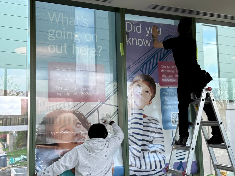 Optically clear overlaminate being applied over installed perforated window film on a pedestrian bridge in Akron