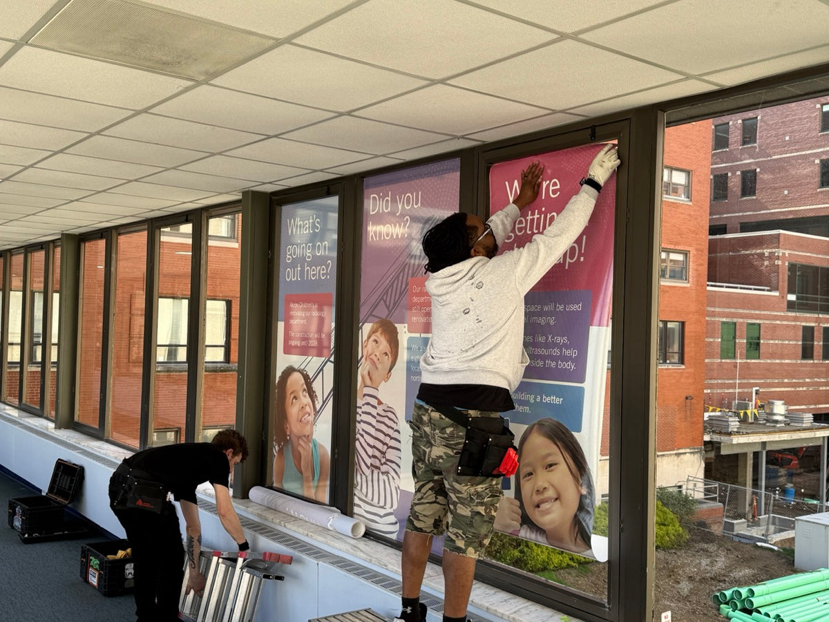 DG Creativ Installers applying window perf graphics with an optically clear over laminate on one of Akron Children's Hospital pedestrian bridges