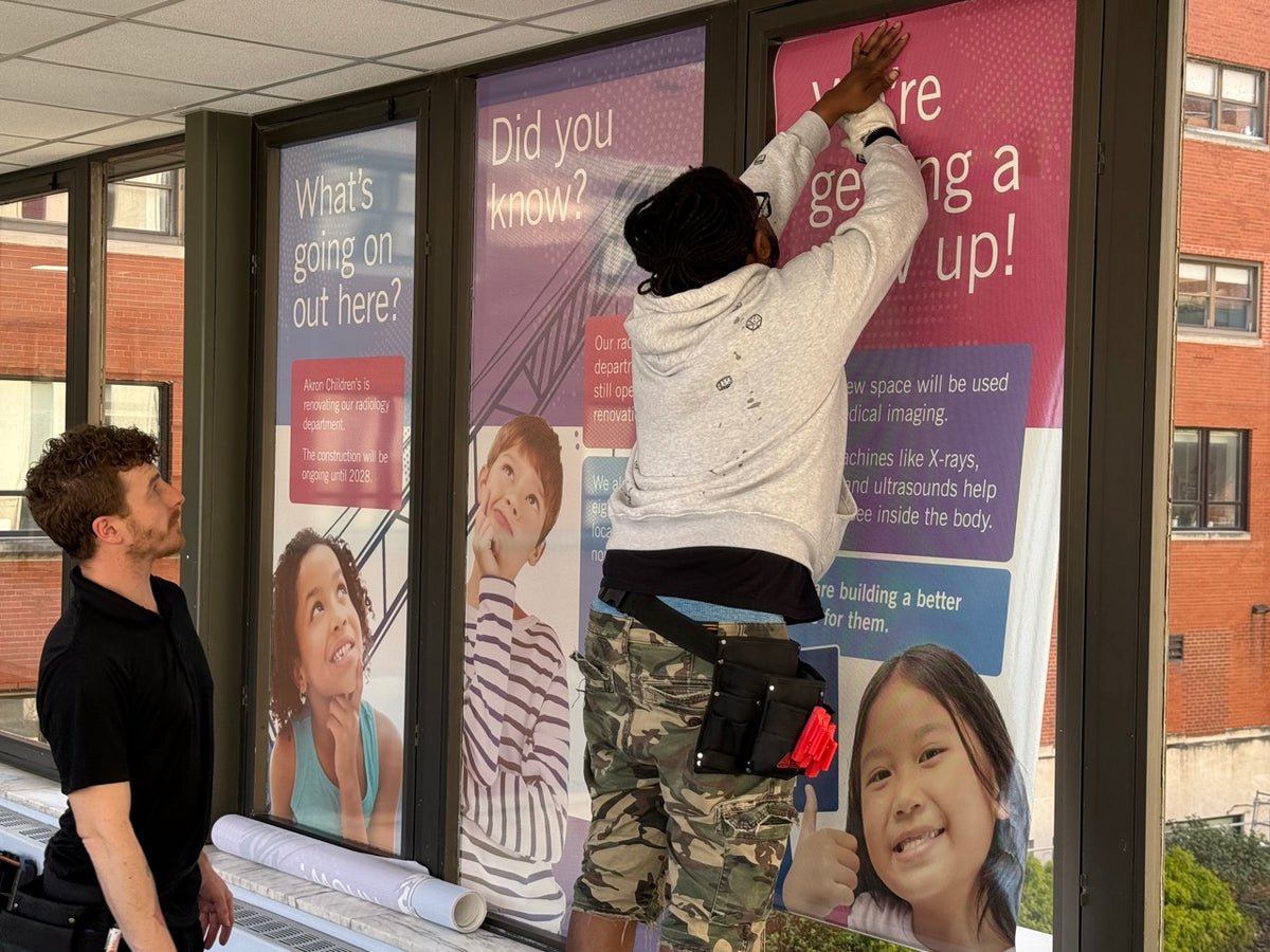 DG Creativ Installers applying window perf graphics with an optically clear over laminate on one of Akron Children's Hospital pedestrian bridges